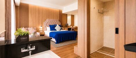 Habitación de hotel moderna con una bañera grande, zona de ducha independiente, cama con ropa de cama azul y pared de paneles de madera.