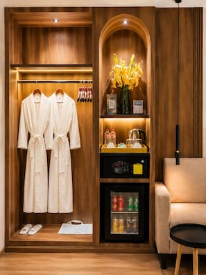 A hotel room with a wooden vanity, a minibar, a seating area, and a robe rack. - Harmony Phnom Penh Hotel (Phnom Penh)