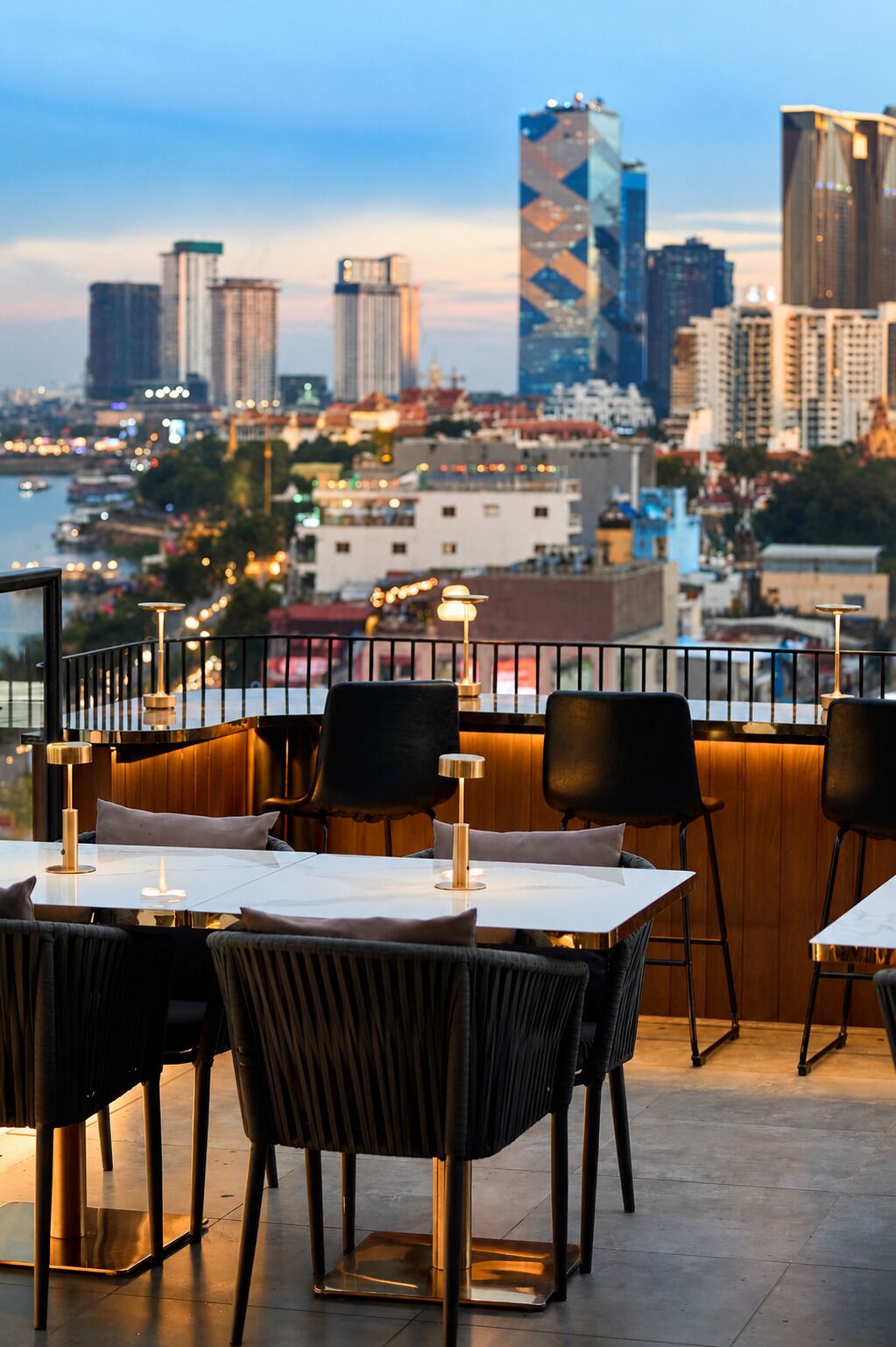 An outdoor dining area with tables and chairs, a city view, and a railing.