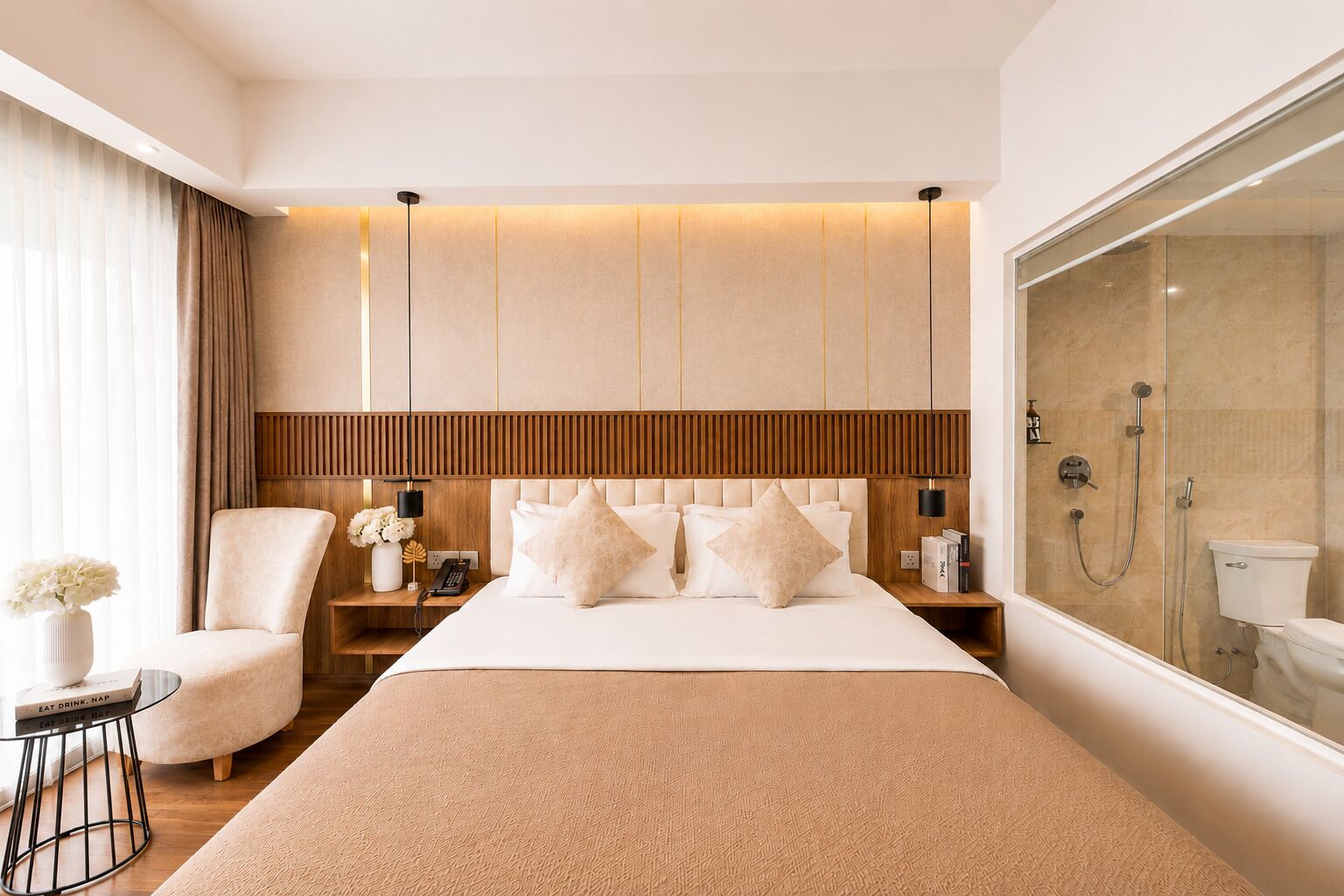 Una moderna camera d'albergo con un letto grande, un angolo salotto con una poltrona, un comodino con una lampada e un'ampia finestra.