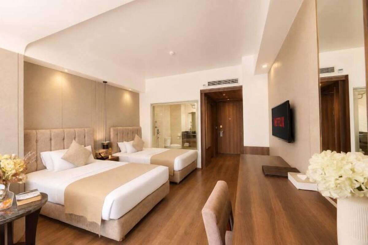 A hotel room with two beds, a TV, a desk, and a mirror.
