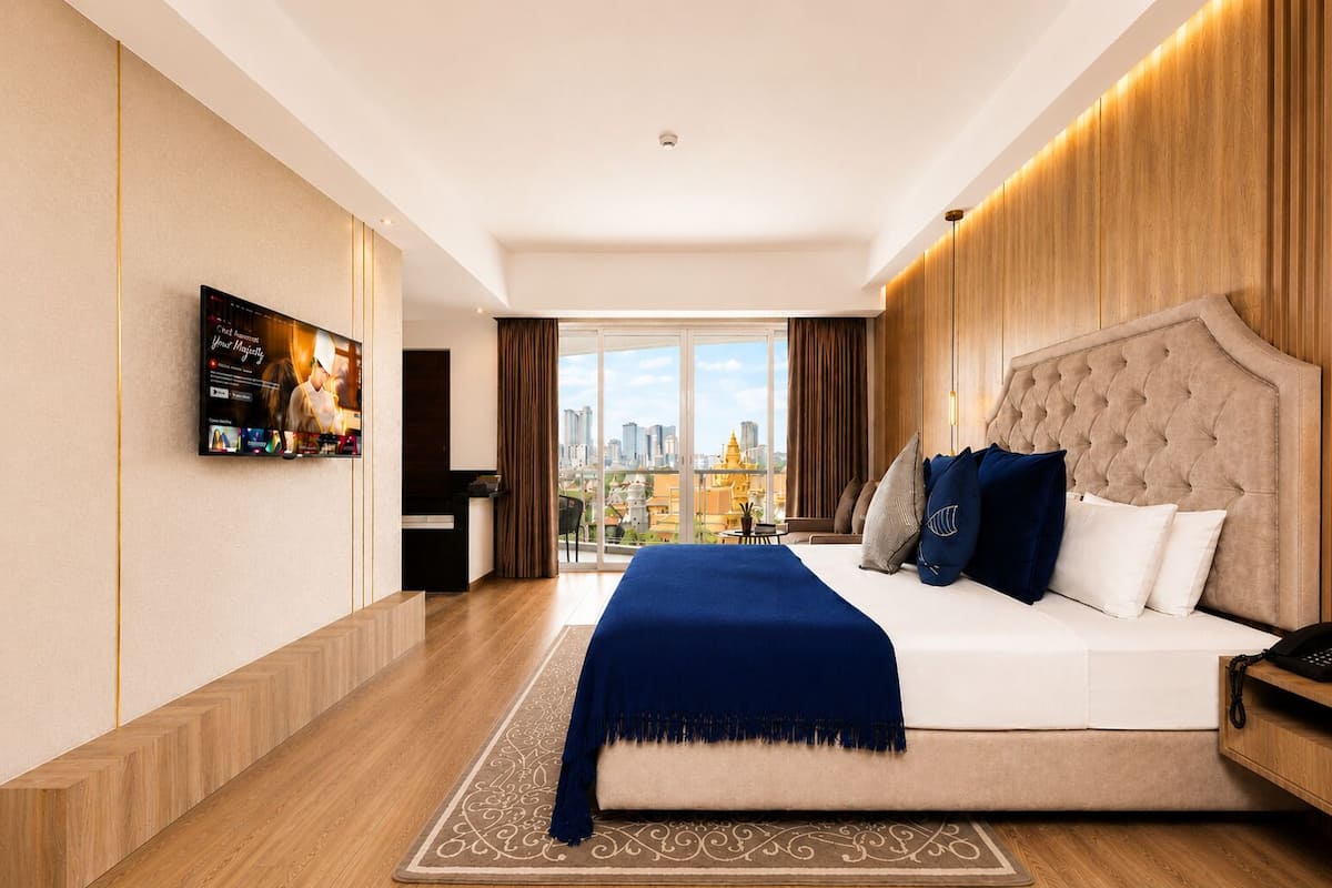 A modern hotel room with a large bed, a TV mounted on the wall, and a city view.