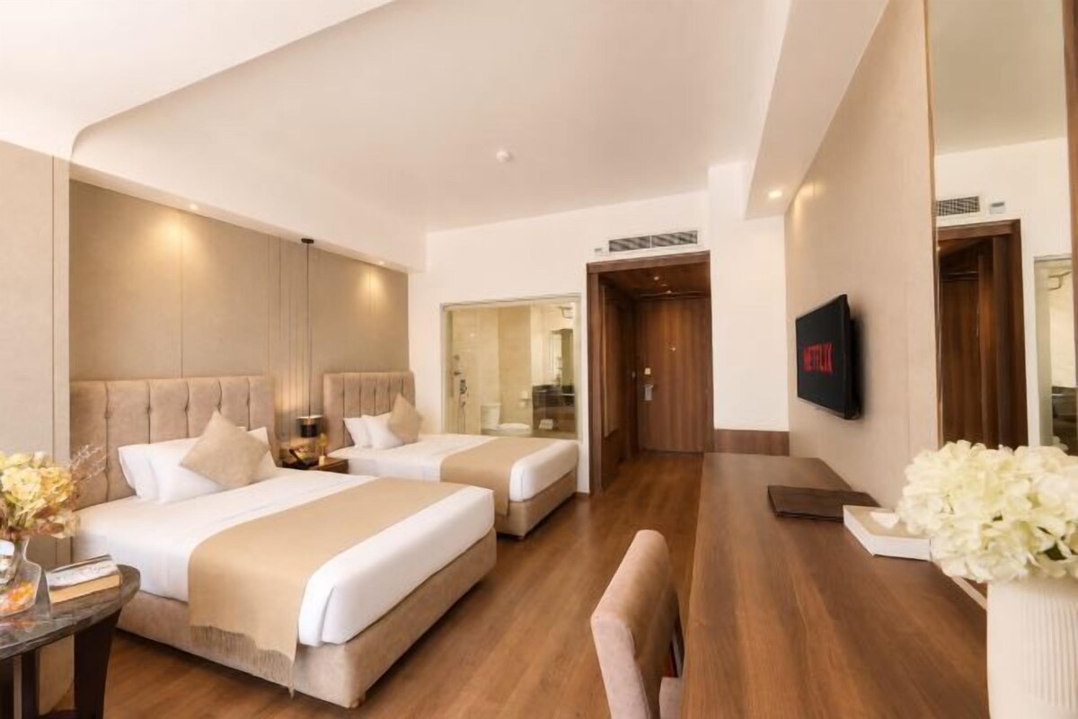 A hotel room with two beds, a TV, a desk, and a mirror.