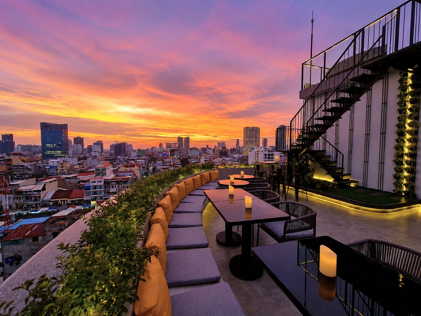 Une terrasse sur le toit, aménagée avec des sièges, un escalier et une vue imprenable sur la ville au coucher du soleil.