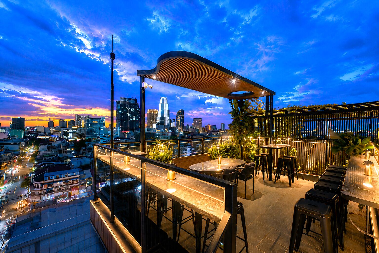 A rooftop bar with a city view, outdoor seating, and a wooden pergola.