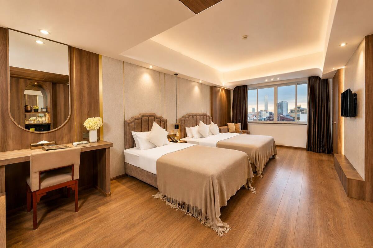 A hotel room with two beds, a desk, a mirror, and a city view.