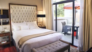 A hotel room with a large bed, a bedside table with a lamp, a small table with chairs, and a view of the outdoors through a glass door. - Atiq Boutique Hotel (Cusco)
