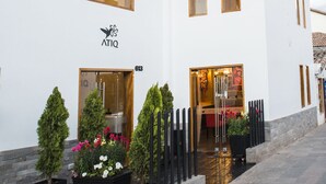 A white building with a tiled roof, a sign reading "ATIQ", and a number "613" on the facade. There are potted plants and a small outdoor area with a bench. - Atiq Boutique Hotel (Cusco)