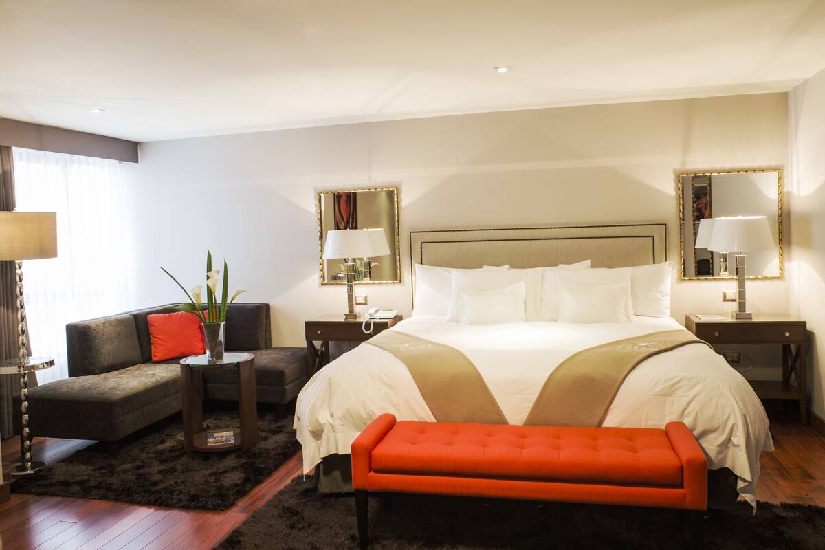 A hotel room with a large bed, a sofa, a small table, and a bench.