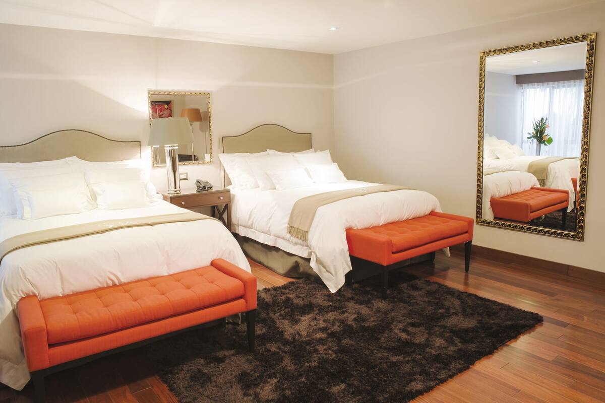 A hotel room with two beds, a large mirror, and a black rug.