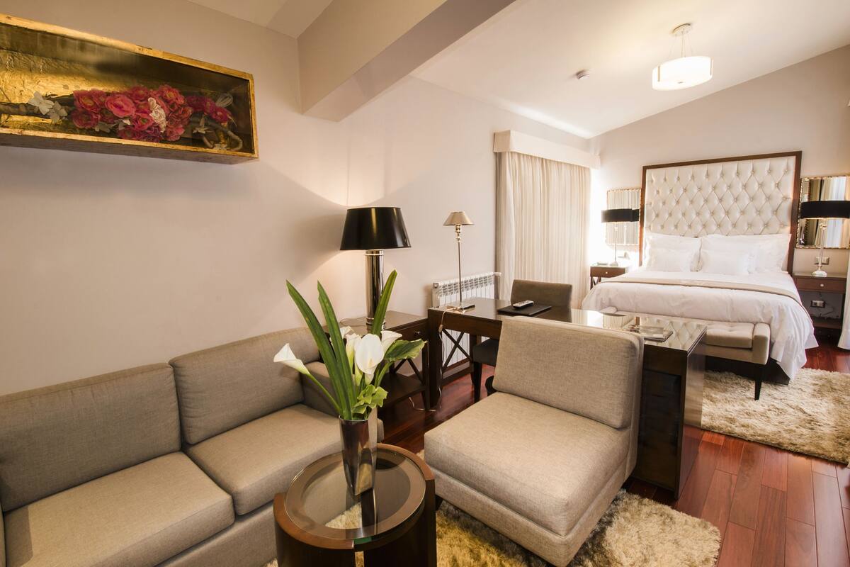 A modern hotel room with a large bed, a sofa, a coffee table, and a painting on the wall.
