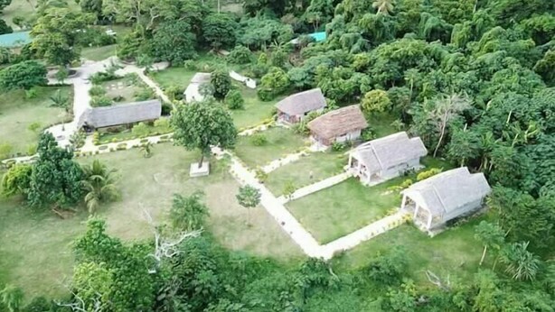 Vista aérea de una zona rural con varias casas de techo de paja rodeadas de abundante vegetación.