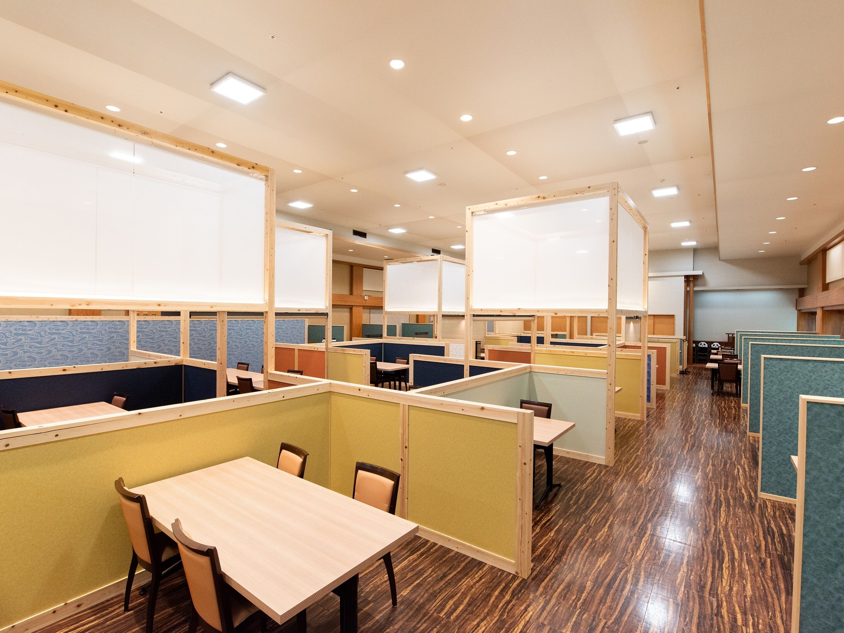 Un comedor moderno con mesas y sillas de madera, cabinas separadas y piso de madera pulida.
