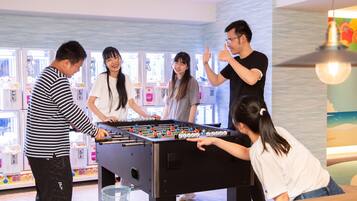 A group of people playing foosball in a brightly lit room with a view of the sea through the windows.