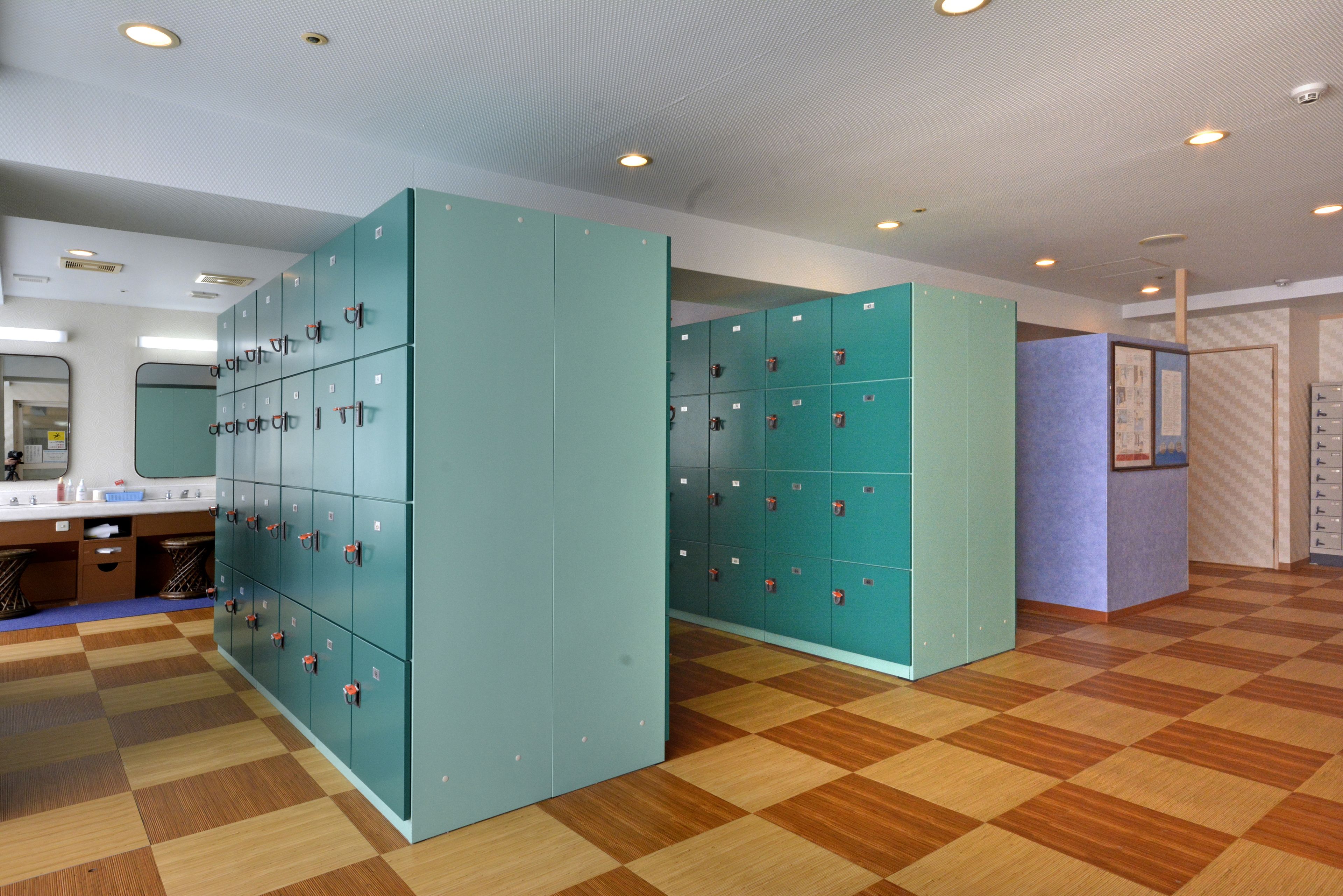 A locker room with teal lockers, a wooden checkered floor, and a mirror above the sink.