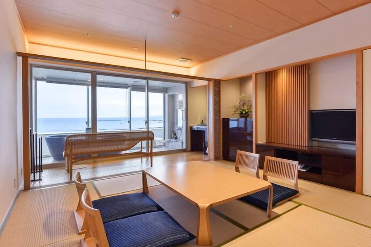 A modern room with a large sliding glass door leading to a balcony, a wooden dining table with chairs, a TV, and a small plant.