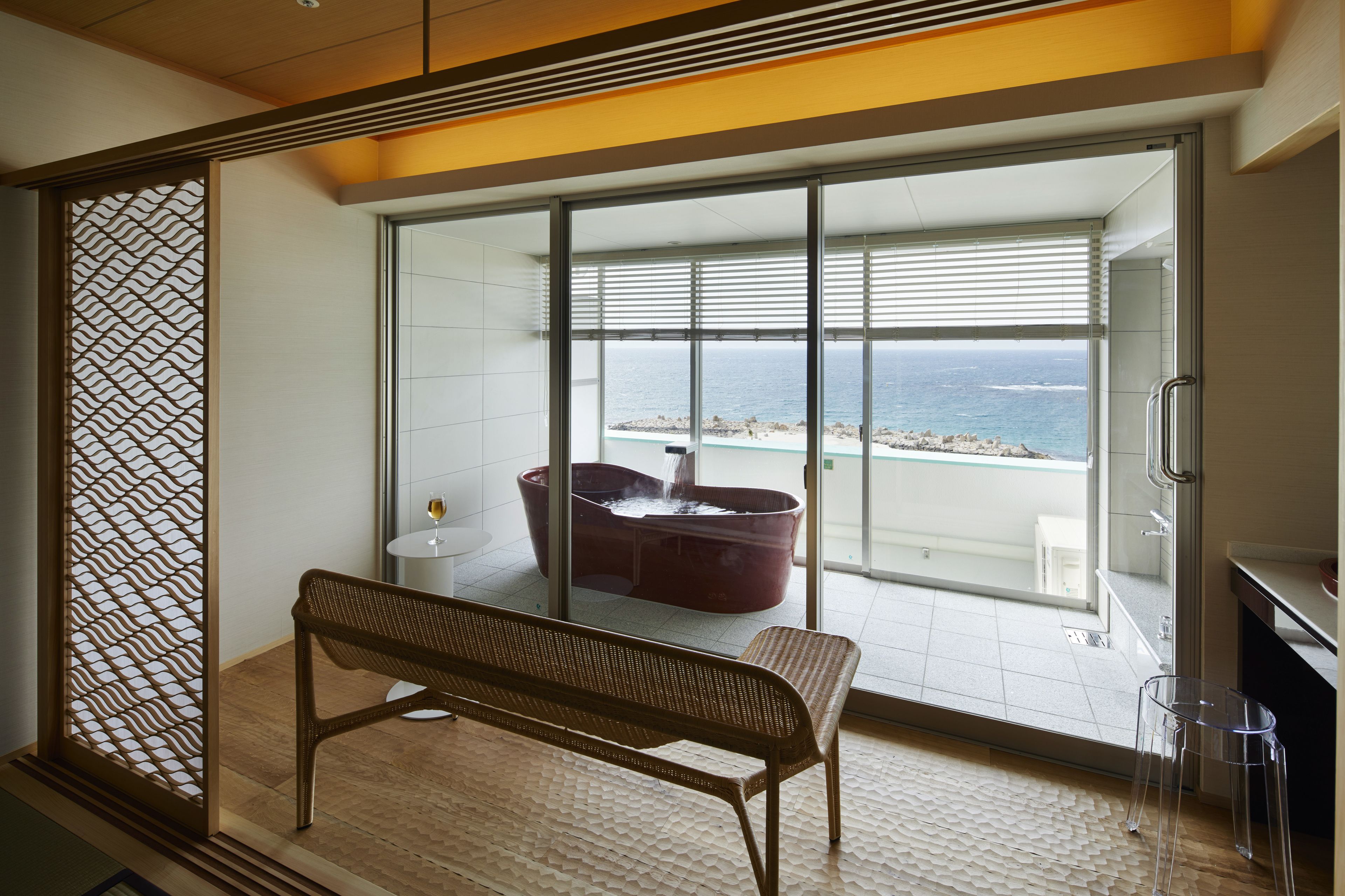 A modern room with a large sliding glass door leading to a balcony with a view of the sea.