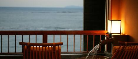 A balcony with wooden chairs and a hot tub, overlooking the ocean.
