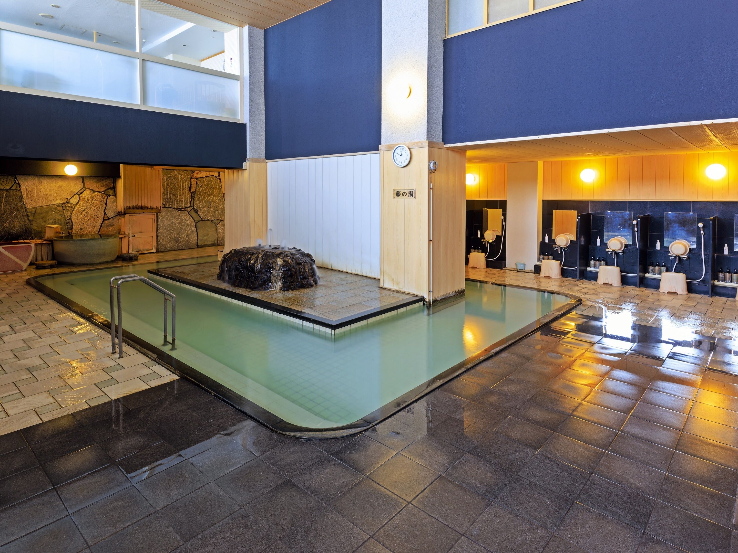 A modern indoor pool area with a stone hot tub, a changing room, and a sauna.