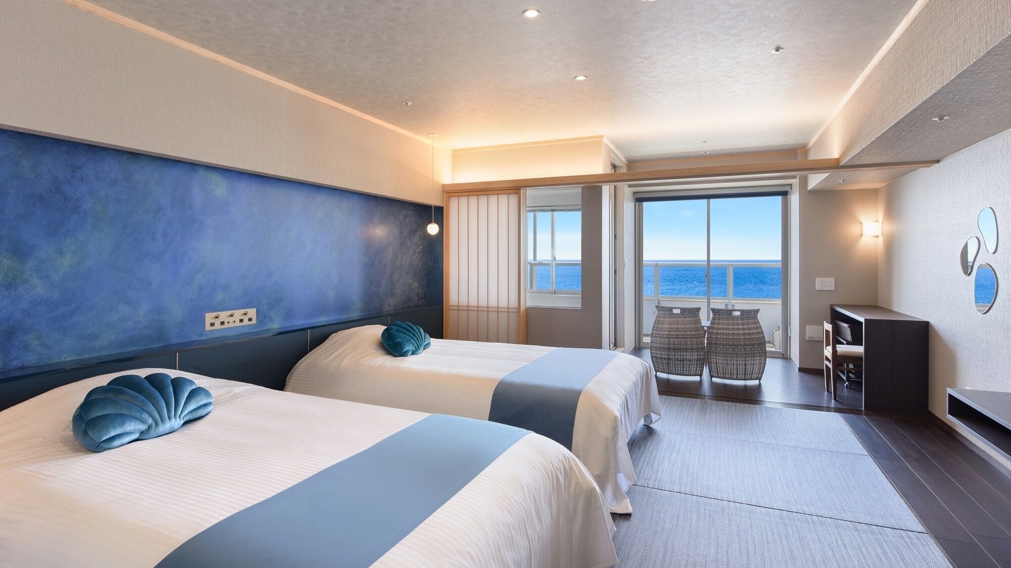 A hotel room with two beds, a balcony with a view of the sea, and a seating area with a table and chairs.