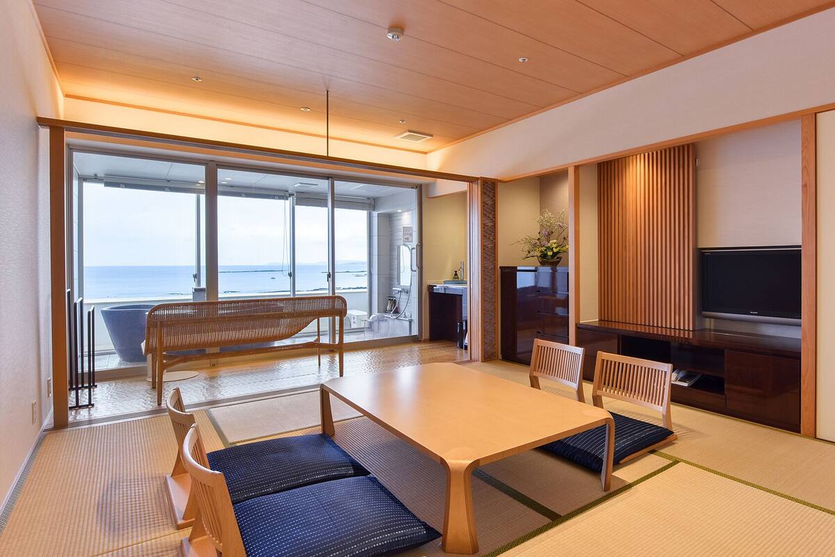 Una camera moderna con un tavolo di legno, sedie, un televisore e vista sul mare.