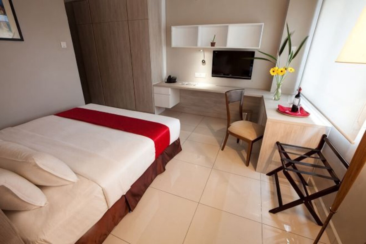 A hotel room with a bed, desk, chair, and a TV.