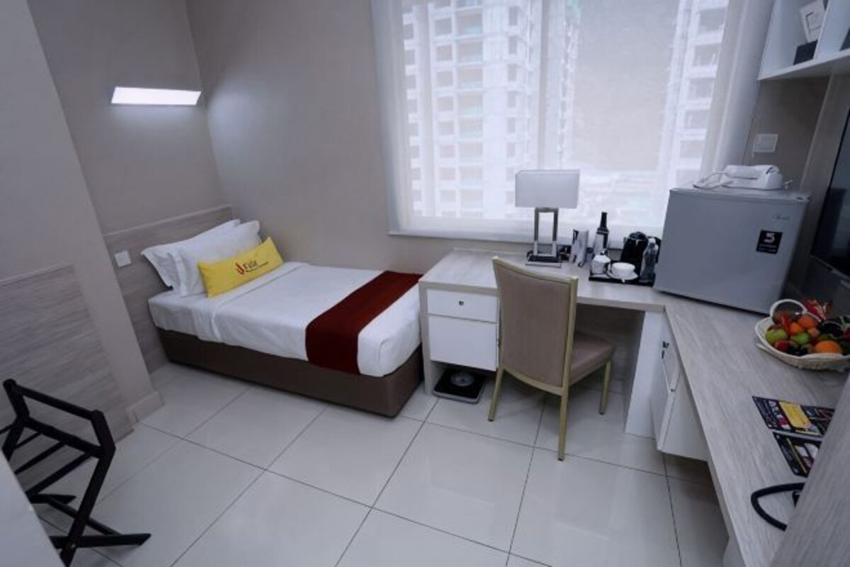 A hotel room with a bed, desk, chair, and a small refrigerator.