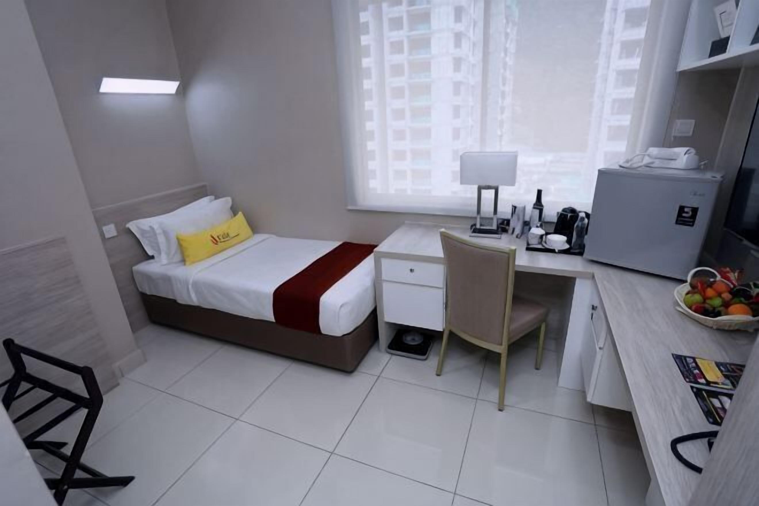A hotel room with a bed, desk, chair, and a small refrigerator.