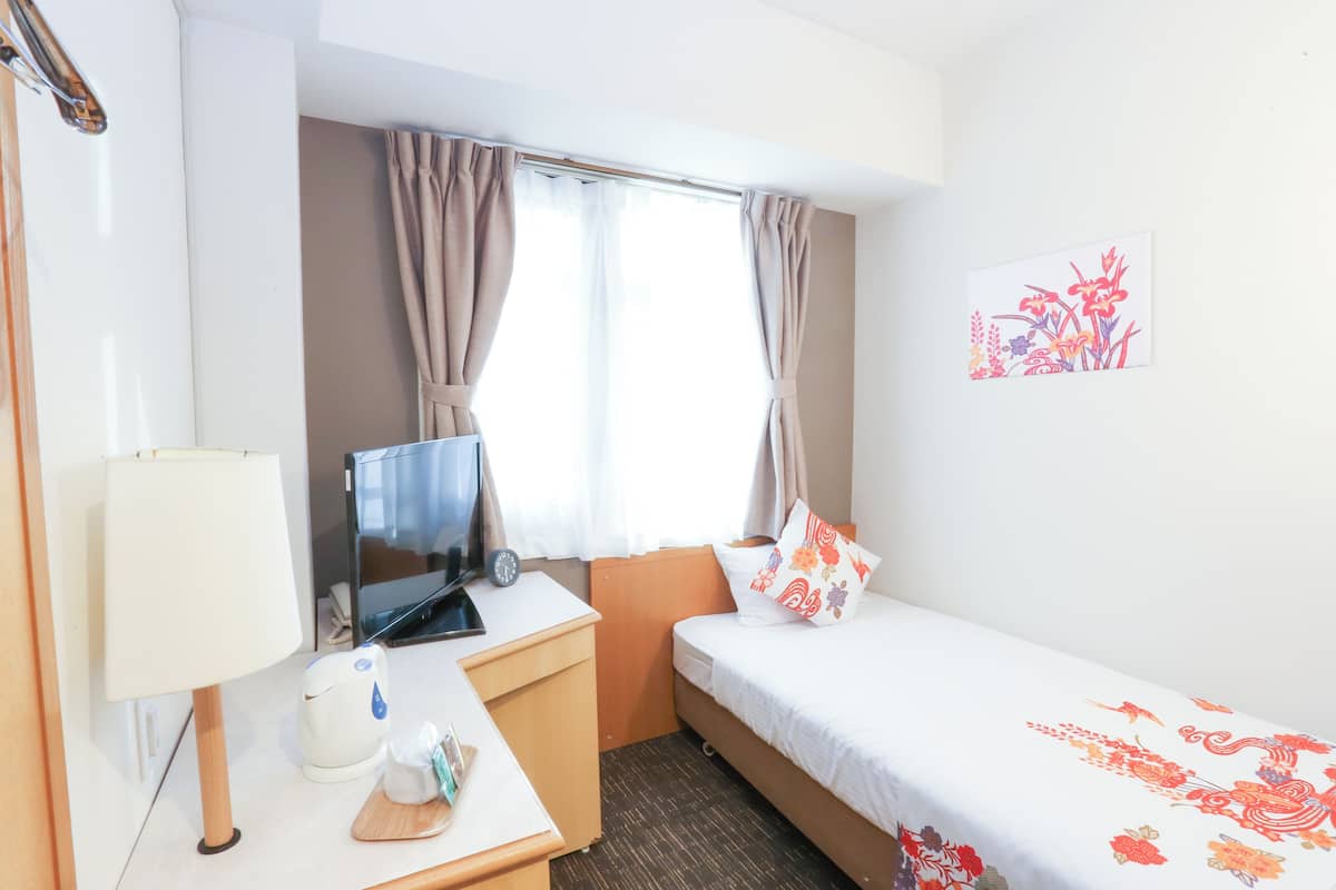 A hotel room with a bed, a desk with a lamp, a television, and a window with curtains.