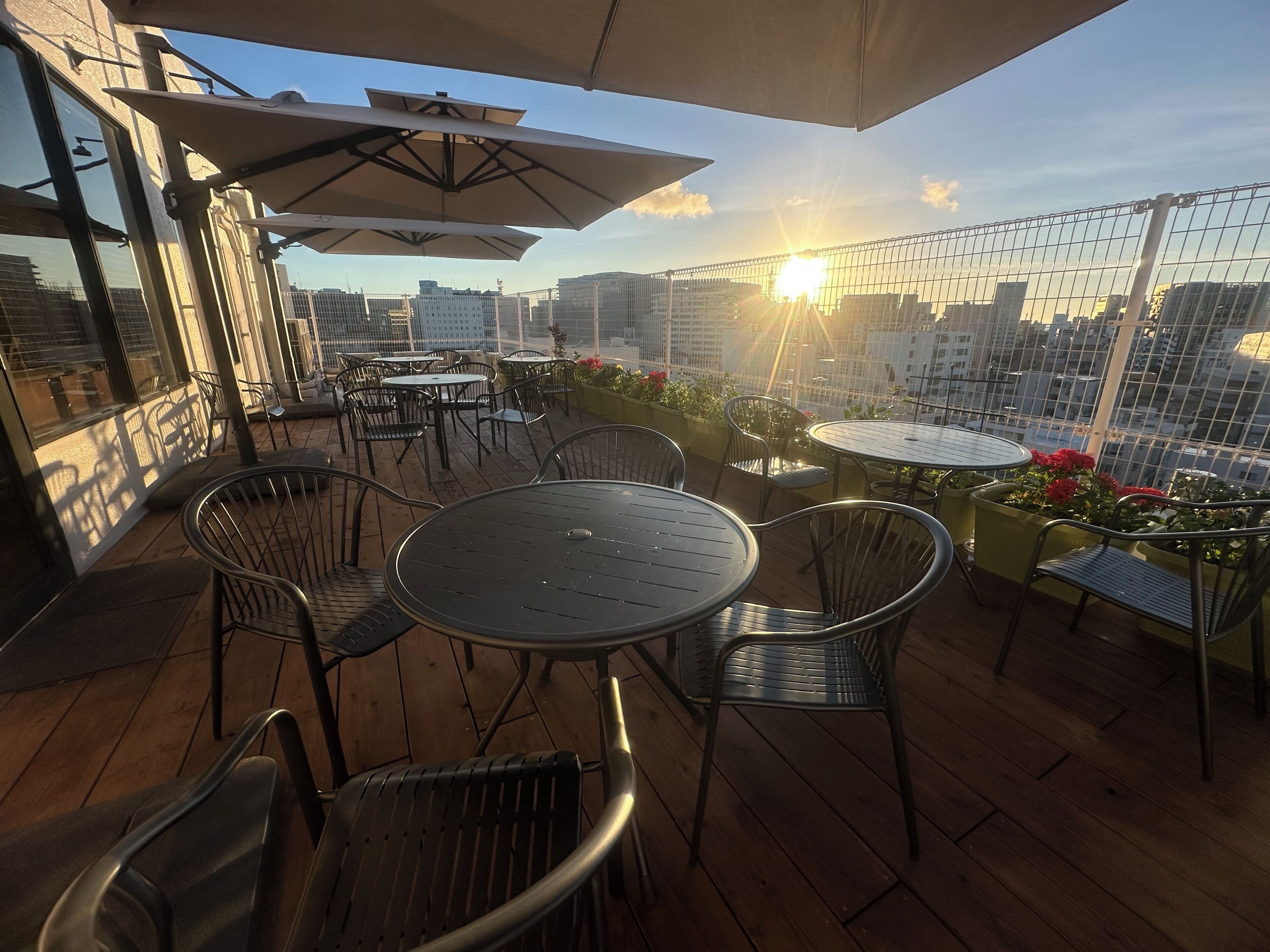 An outdoor seating area with tables and chairs, umbrellas, and a view of the cityscape.