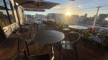 An outdoor seating area with tables and chairs, umbrellas, and a view of the cityscape.