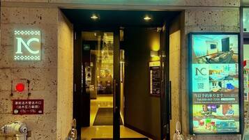 The entrance to HOTEL NAHA CITY on KOKUSAI STREET, featuring a neon sign, a reception desk, and a digital display with room images.