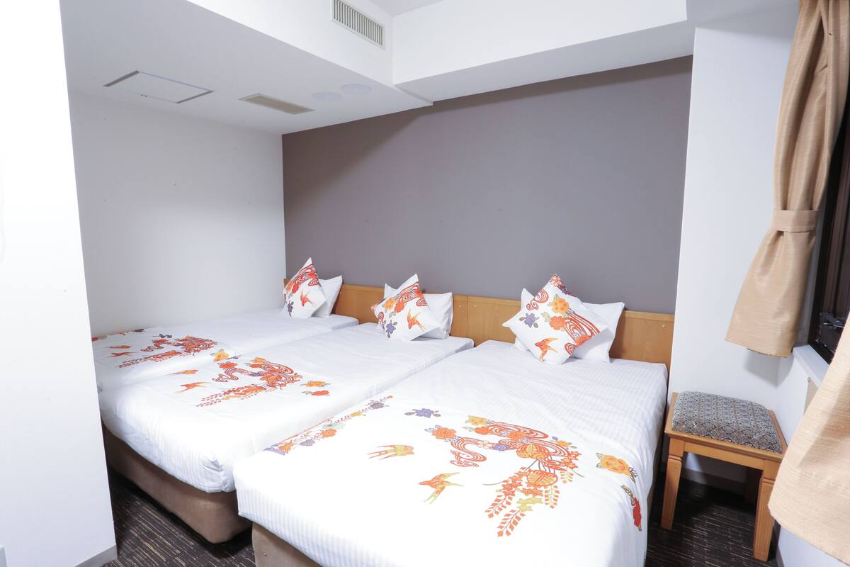 A double bed with floral bedspreads, a wooden headboard, and a small wooden stool.
