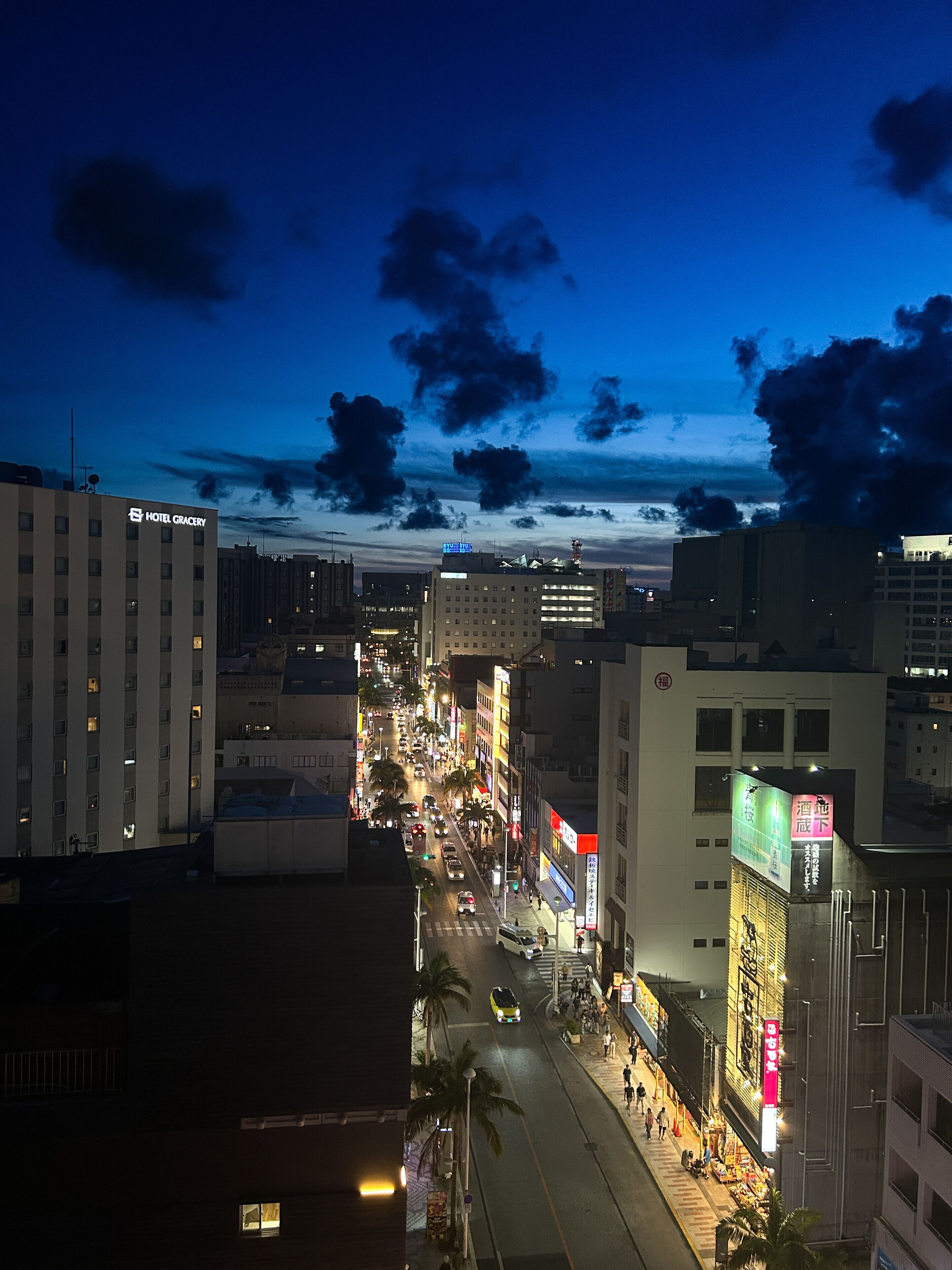 A city street at night with buildings, vehicles, and pedestrians.