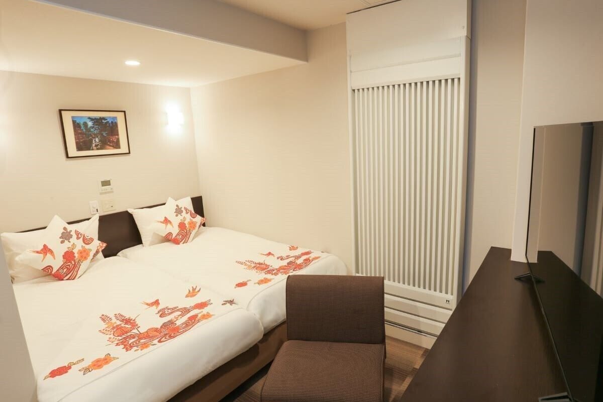 A hotel room with a bed, a desk, a chair, a television, and a window with blinds.