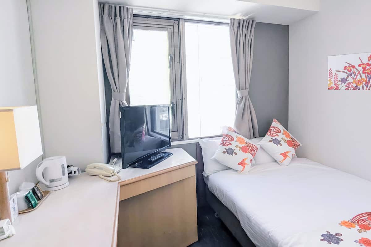 A hotel room with a bed, a desk with a computer, a telephone, and a window with curtains.
