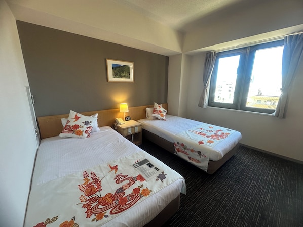 Una habitación de hotel con dos camas, una mesita de noche con lámpara, un cuadro enmarcado en la pared y una ventana con cortinas.