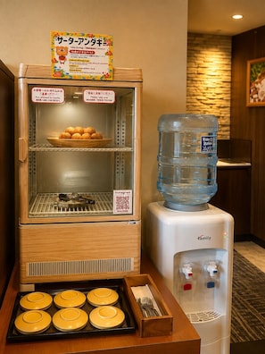 A self-service food station with a rice cooker, a water dispenser, and a tray of yellow plates. - Hotel Naha City -Kokusai Street- (Naha)