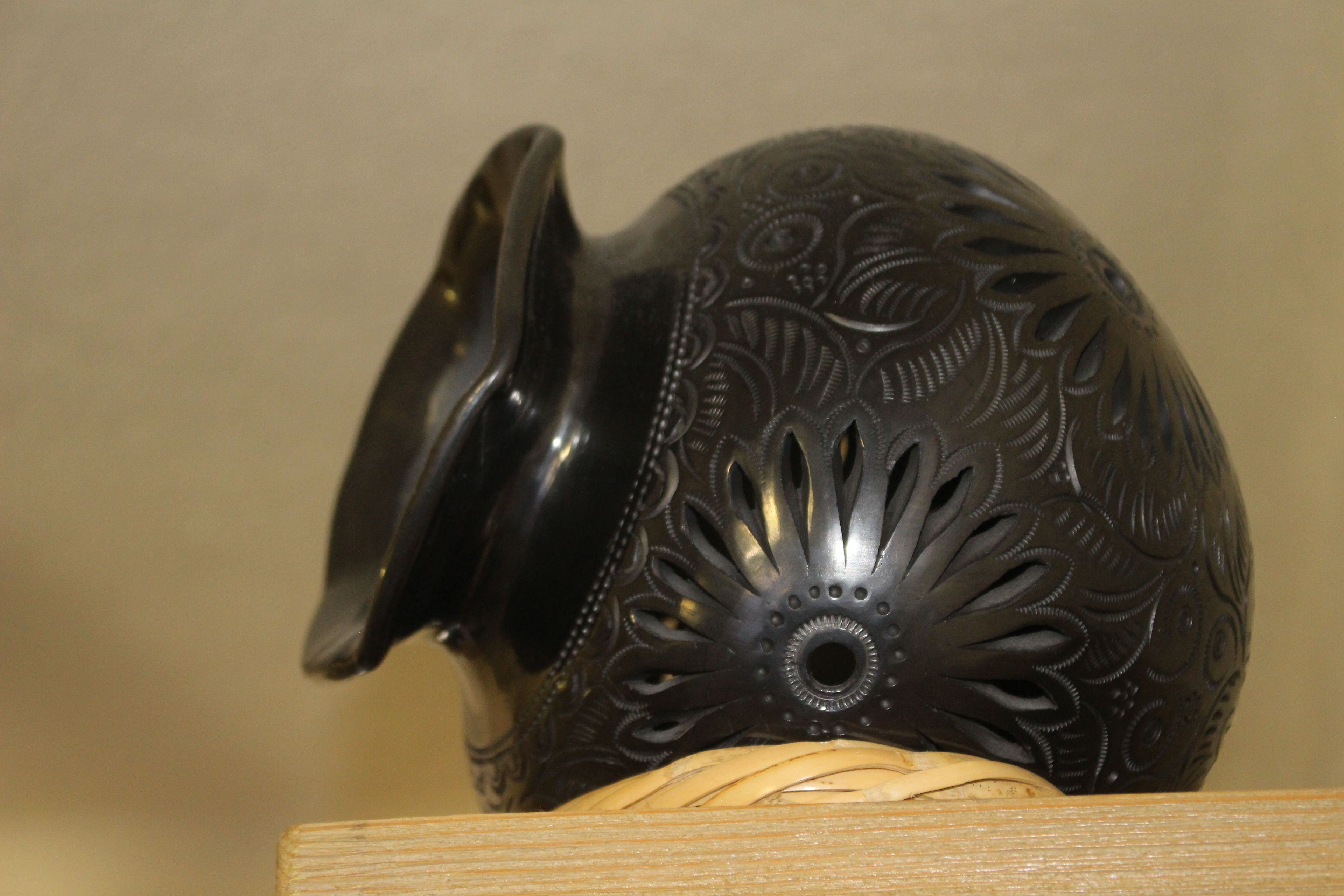 A dark, intricately patterned ceramic pitcher with a lid, placed on a wooden surface.