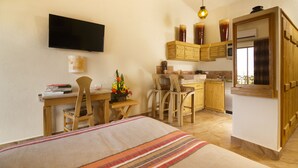 Une pièce de taille modeste comprenant un lit, un bureau, une chaise, un téléviseur et un coin cuisine.