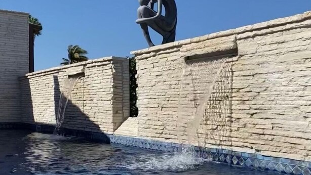 Un muro de piedra con una fuente de agua y una escultura.