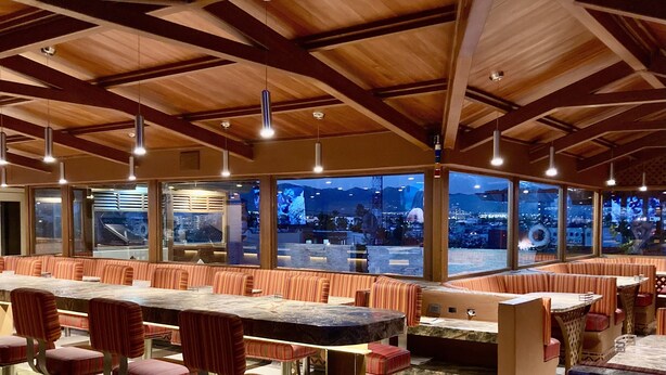 Un restaurant avec de hauts plafonds, des poutres en bois et de grandes fenêtres donnant sur la ville.