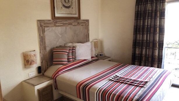 Una habitación de hotel ordenada, con una cama grande, cabecero, mesitas de noche y una ventana con cortinas.