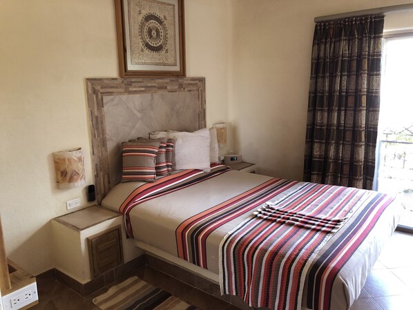 A neatly arranged hotel room with a large bed, a headboard, bedside tables, and a window with curtains.