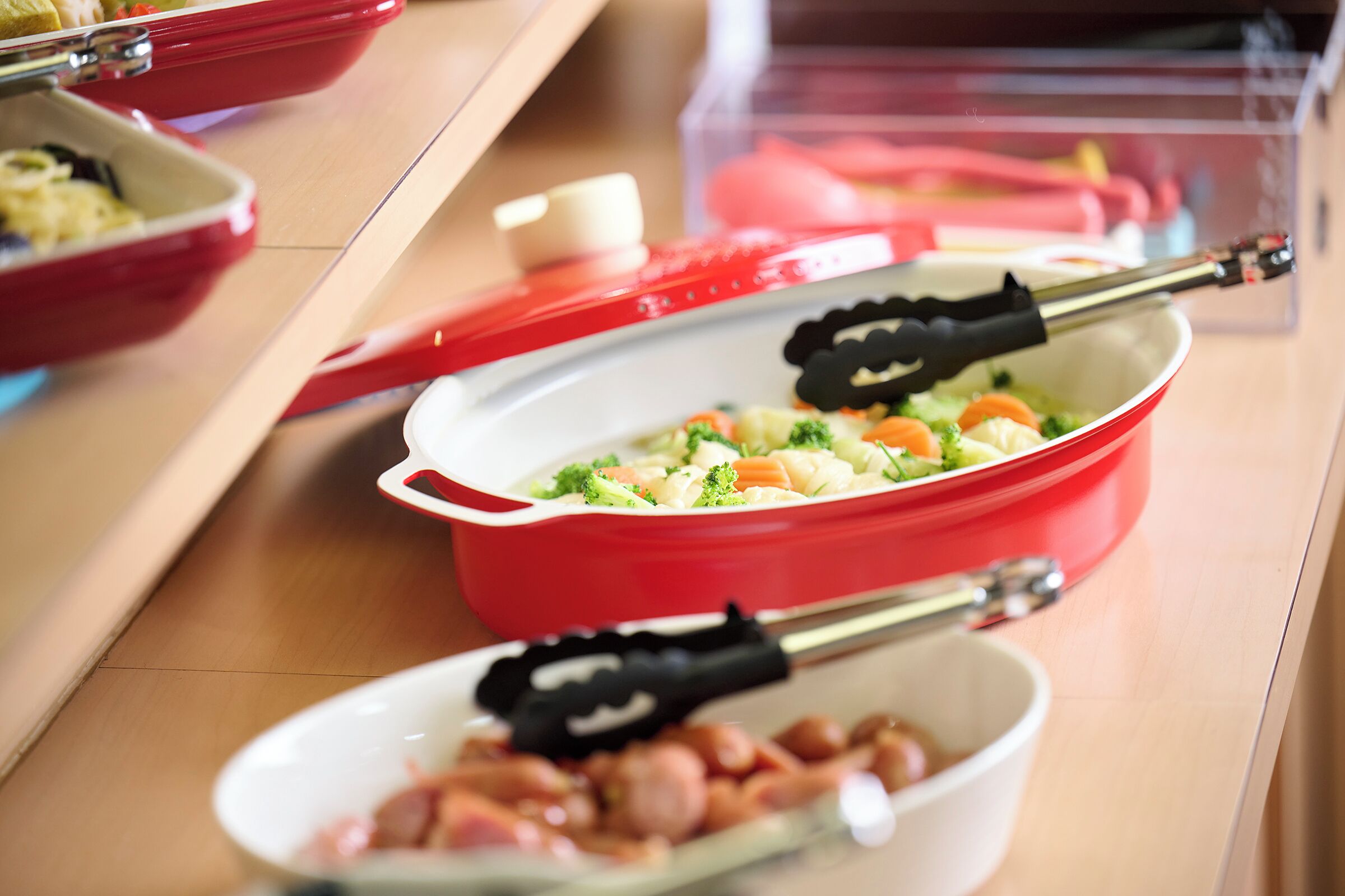 Una mesa de buffet con diversos platos, incluyendo un recipiente rojo con un guiso de verduras y un bol blanco con carne.