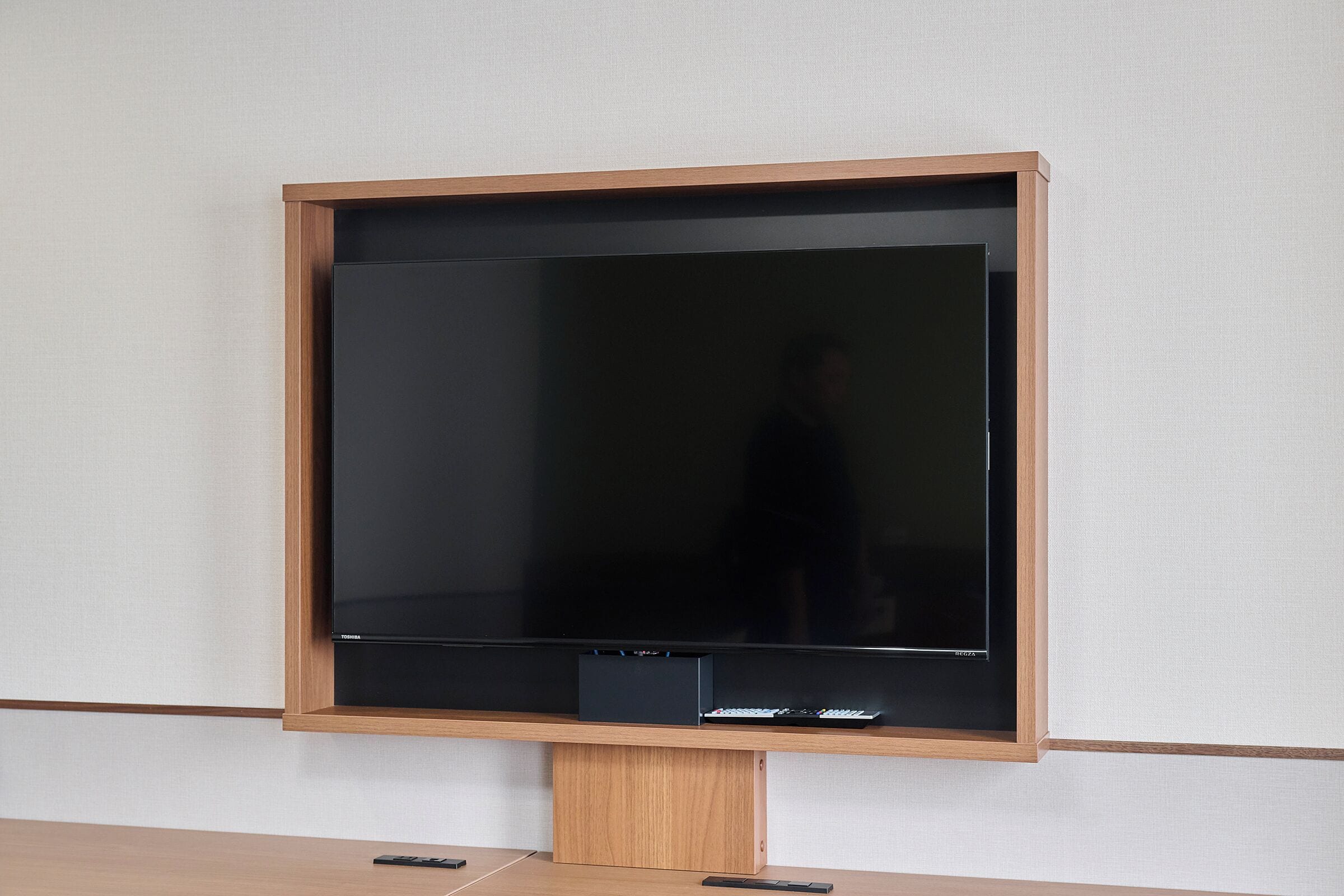 Un televisor montado sobre un soporte de madera frente a una pared lisa.