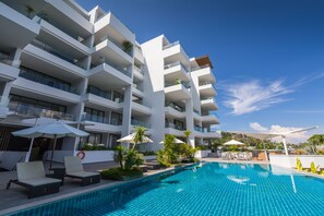 Um hotel moderno com piscina, várias varandas e áreas de estar ao ar livre.