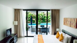 A hotel room with a bed, a TV, a desk, and a view of a swimming pool. - Sansuri Resort Phuket (Choeng Thale)