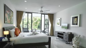 A modern hotel room with a large bed, a ceiling fan, a television, and a statue. - Sansuri Resort Phuket (Choeng Thale)