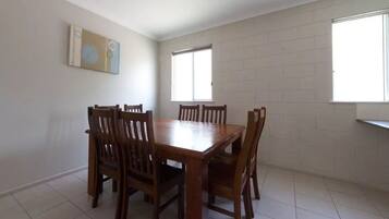 A dining area with a wooden table and chairs, two windows, and a white brick wall.